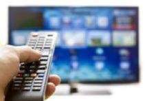Une main tient une télécommande devant un écran de télévision.