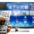 Une main tient une télécommande devant un écran de télévision.